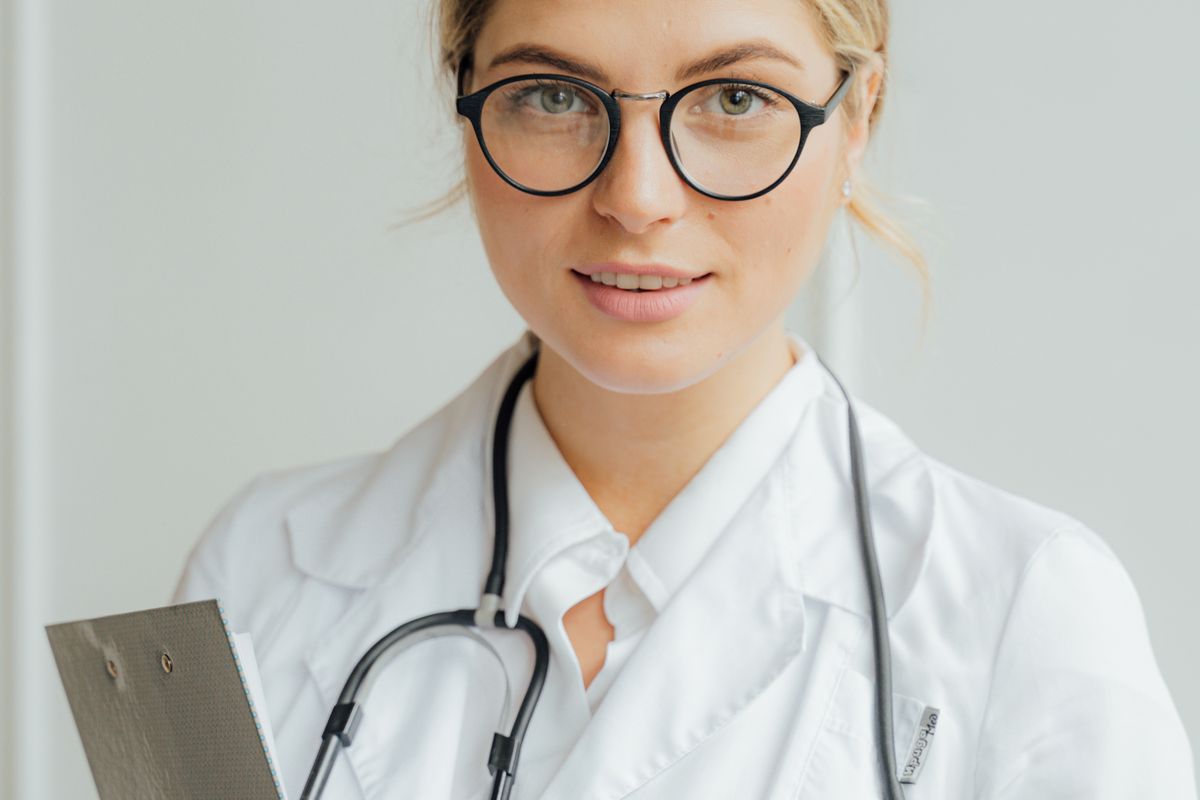 A doctor in a white coat sitting across from a patient, holding a clipboard with a dosage chart, explaining a medication schedule in a bright, modern clinic office